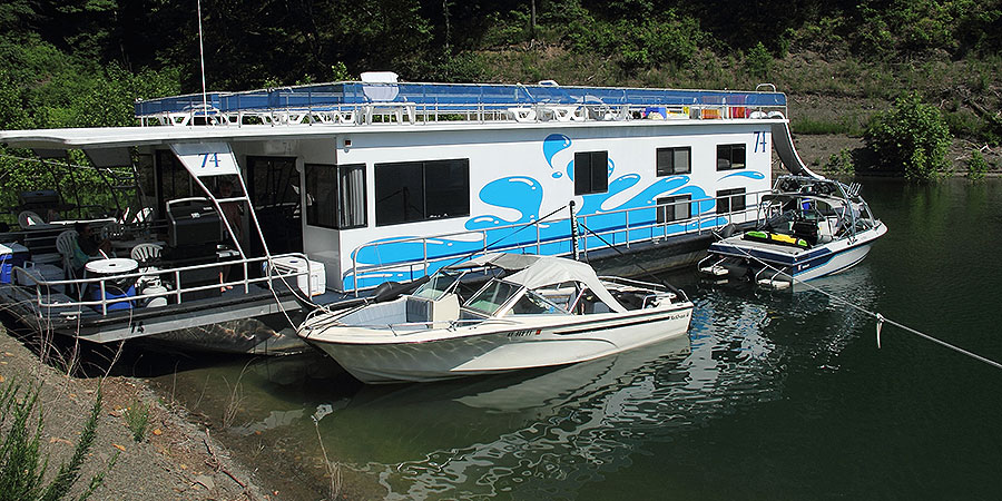 Two boats tied off on the houseboat that docked on the lakes shore.