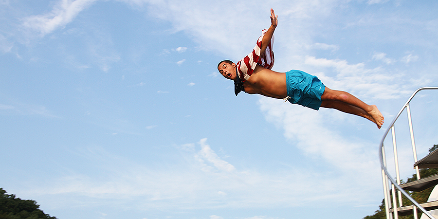 A man jumping of boat with American flag decorated cape.